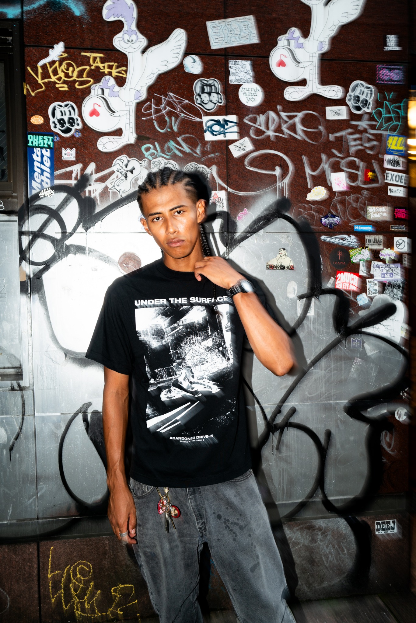 グラフィティの壁の前で黒いUTS Tシャツを着たモデル