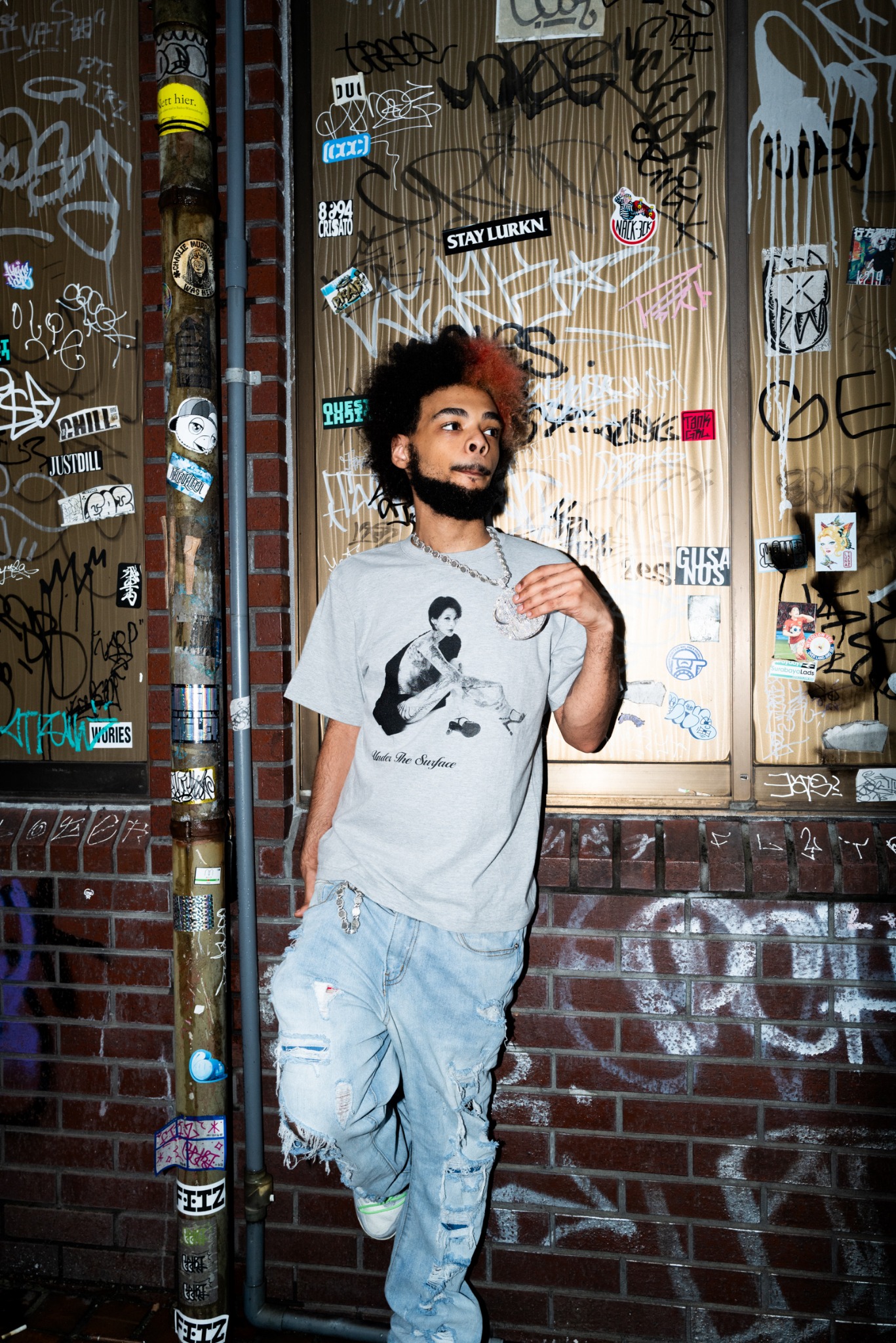 グラフィティの壁の前でグレーのUTS Tシャツを着たモデル